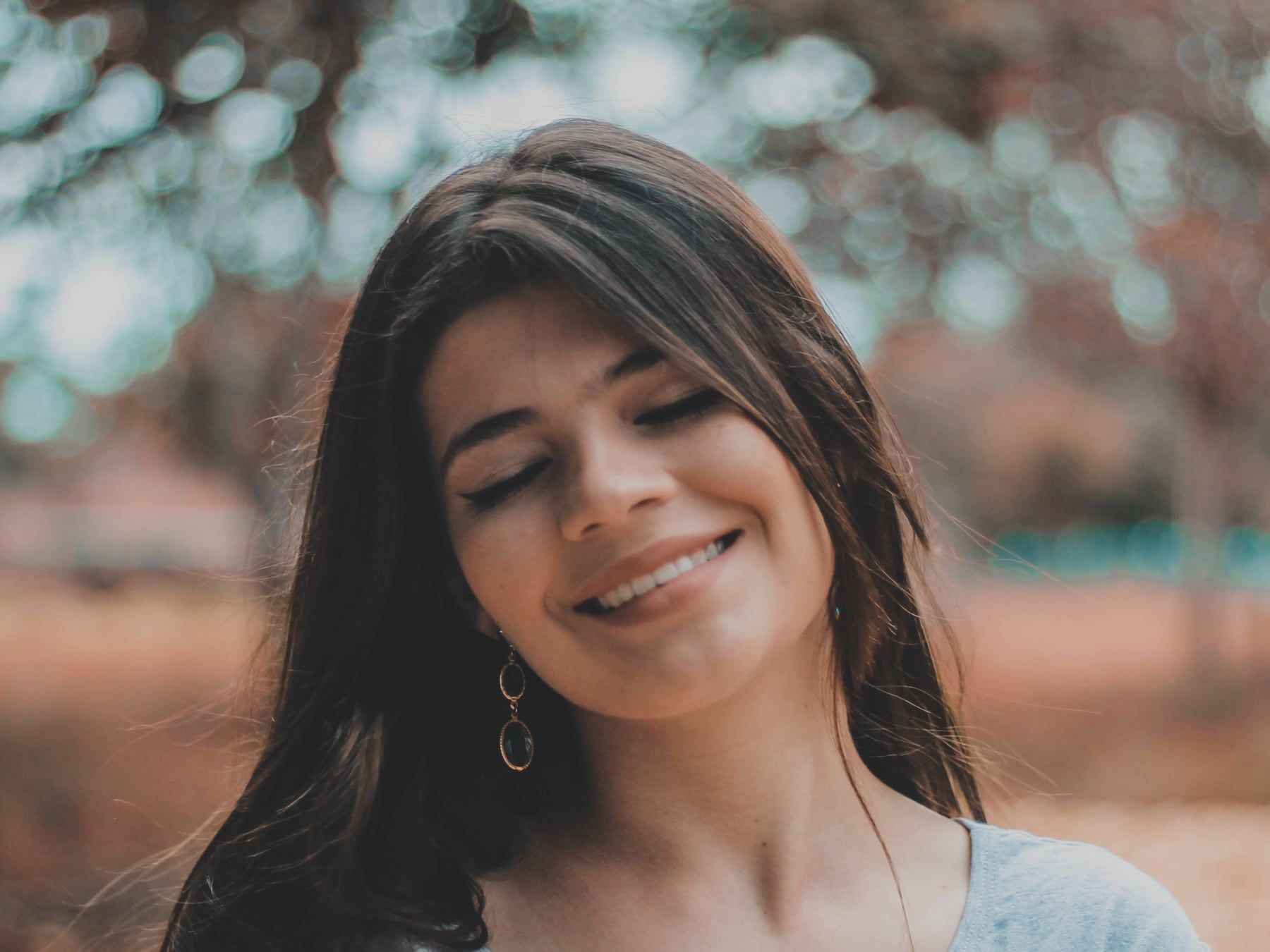 Mujer joven sonriendo con los ojos cerrados, al aire libre.